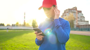 Kadın ve smartphone kablosuz kulaklık ile müzik seçer ve gün batımında stadyumun çalışır. Ağır çekim