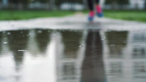 Cerrar la toma en cámara lenta de las piernas de un corredor en zapatillas de deporte. Mujer deportista corriendo al aire libre en un parque, entrando en un charco fangoso . — Vídeos de Stock