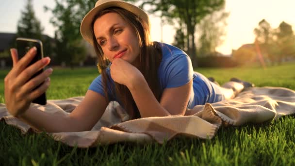 Girl making a selfie lying down on a blanket in the park at sunset — Stock Video