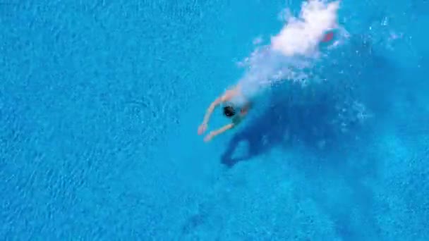 Uitzicht vanaf de top zoals een man in het zwembad duikt en zwemt onder het water — Stockvideo