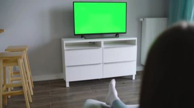 Kadın bir sandalyede oturuyor, yeşil ekran ile Tv izliyor, uzaktan kumanda ile kanal geçiş. Renk anahtarı. Kapalı