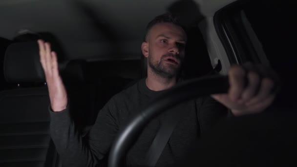Man rijdt in een auto en begint te vloeken en verontwaardigd als hij ziet de knipperende lichten van de politie achter hem 's nachts — Stockvideo