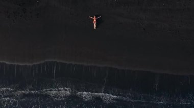 Sörf çizgisinde siyah bir plajda uzanan kırmızı mayo giymiş bir kadının en iyi görüntüsü. Tenerife adasının kıyıları, Kanarya Adaları, İspanya.