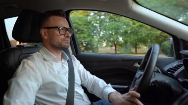 Güneşli havalarda araba kullanan gözlüklü ve beyaz gömlekli sakallı adam. Yan görünüm