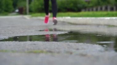 Spor ayakkabılı bir koşucunun bacakları. Spor kadını dışarıda koşuyor, çamurlu su birikintisine giriyor. Yağmurda koşan, su sıçratan tek koşucu. Yavaş çekim
