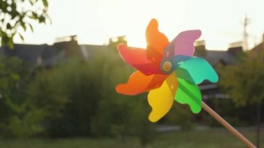 Plastik gökkuşağı yel değirmeni bulanık evlerin ve günbatımının arka planında döner. Varoşlar Konsepti