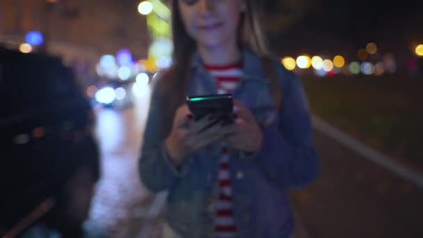 Mulher usa um smartphone enquanto caminha pelas ruas da cidade da noite — Vídeo de Stock