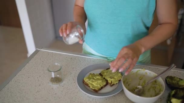 Kvinna matlagning avokado rostat bröd, strör det med salt och kryddor — Stockvideo