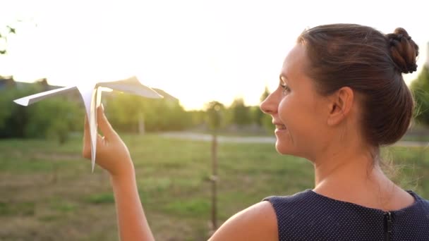 Vrouw lanceert papieren vliegtuig tegen zonsondergang achtergrond. Dromen van reizen of het beroep van stewardess. Langzame beweging — Stockvideo
