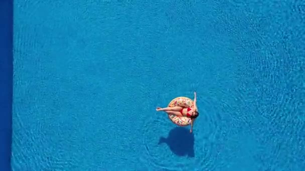Εναέρια άποψη μιας γυναίκας με κόκκινο μπικίνι ξαπλωμένη σε ένα ντόνατ στην πισίνα — Αρχείο Βίντεο
