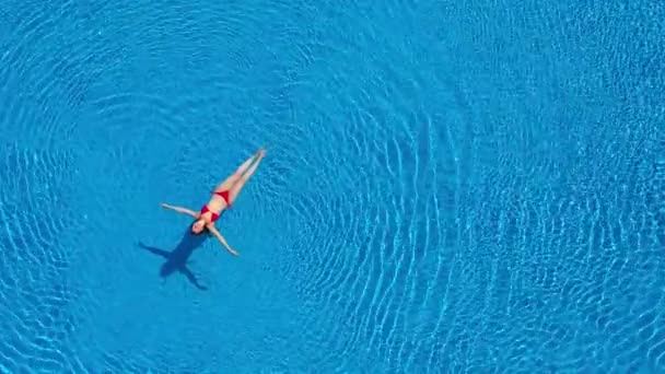Вид сверху на женщину в красном купальнике, плавающую и лежащую на спине в бассейне. Расслабляющая концепция — стоковое видео