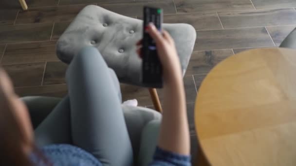 La mujer está sentada en una silla, viendo la televisión con una pantalla verde, cambiando los canales con un control remoto. Clave de croma. En interiores — Vídeo de stock