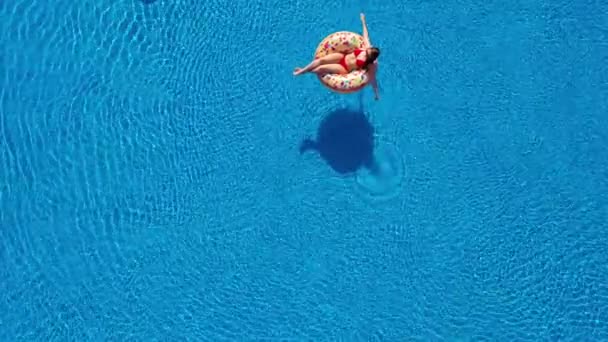 Veduta aerea di una donna in bikini rosso sdraiata su una ciambella in piscina — Video Stock