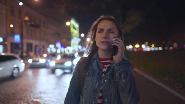 Attraktive Frau, die auf dem Smartphone spricht, während sie durch die Straßen der Abendstadt läuft — Stockvideo