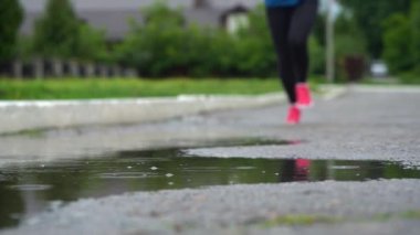Spor ayakkabılı bir koşucunun bacakları. Spor kadını dışarıda koşuyor, çamurlu su birikintisine giriyor. Yağmurda koşan, su sıçratan tek koşucu. Yavaş çekim