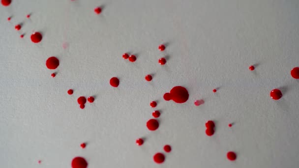 Dessin avec un pinceau sur papier blanc avec aquarelle rouge en gros plan. D'abord, des éclaboussures de peinture rouge volent sur le papier, puis le pinceau peint le fond 