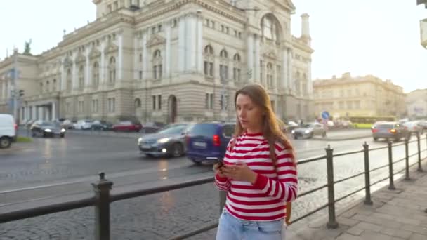 日没時にスマートフォンを使って古い通りを歩いている女性。コミュニケーション、ソーシャルネットワーク、オンラインショッピングの概念 — ストック動画