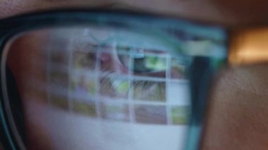 Gözlüklü kadın monitöre bakıyor ve internette sörf yapıyor. Monitör ekranı gözlüklere yansıyor. Çok yakın çekim.