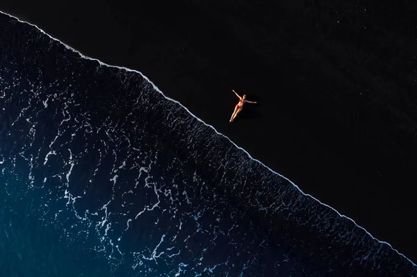 Вид сверху женщины в красном купальнике, лежащей на черном пляже — стоковое фото