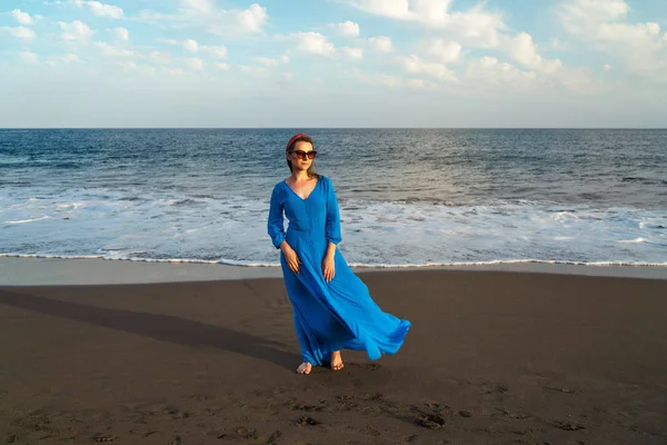 Γυναίκα με όμορφο μπλε φόρεμα σε μια μαύρη ηφαιστειακή παραλία. Ατλαντίδα — Φωτογραφία Αρχείου