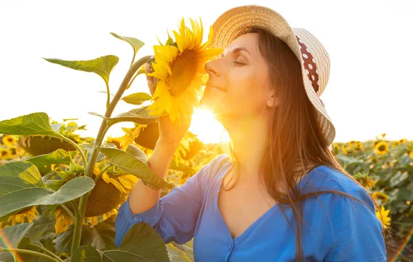 Wanita dengan gaun biru dan topi mengendus bunga matahari di lapangan. Ag — Stok Foto