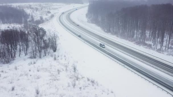 Воздушный обзор движения на дороге, окруженной зимним лесом в снегопаде — стоковое видео