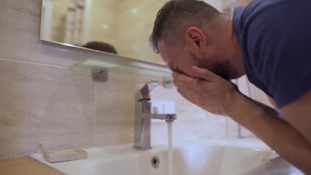 Ochtendhygiëne. De man wast zijn gezicht met schoon water in de badkamer. Langzame beweging — Stockvideo