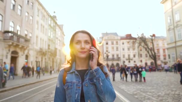 Kvinnan går ner på en gammal gata och pratar i mobilen vid solnedgången. Kommunikationskoncept Långsamma rörelser — Stockvideo