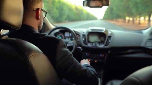 Hombre barbudo vestido formalmente en gafas que conducen un coche en tiempo soleado. Vista desde el asiento trasero de un coche — Vídeos de Stock