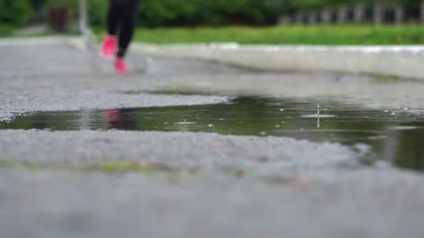 Benen på en löpare i sneakers. Sport kvinna jogging utomhus, kliva in lerig pöl. Singel löpare kör i regn, vilket gör Splash. Slow motion — Stockvideo