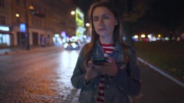 Akıllı telefon kullanan bir kadın ve şehrin sokaklarında yürürken çevreyi göz önünde bulundurur.