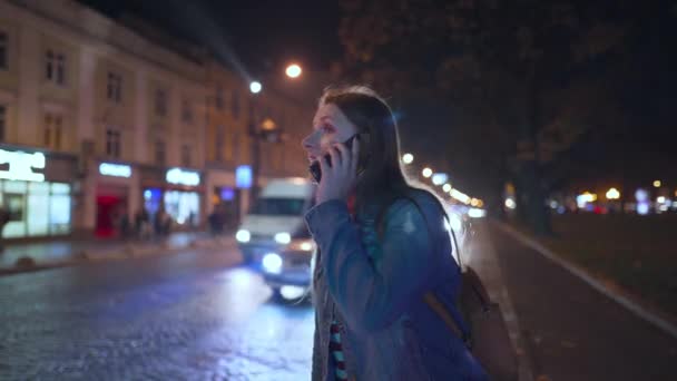 Frau spricht sehr emotional mit ihrem Freund auf einem Smartphone, sieht ihn und winkt ihn freudig auf der Straße der Abendstadt — Stockvideo