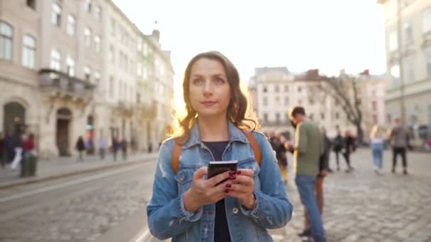 Mujer caminando por una calle vieja usando smartphone al atardecer. Comunicación, redes sociales, concepto de compras en línea . — Vídeo de stock