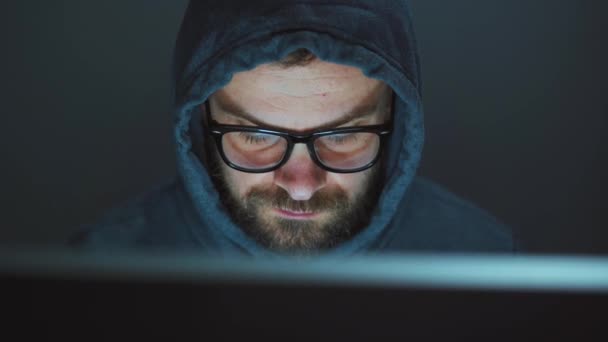 头罩里的男性黑客和眼镜在一间黑暗的办公室的电脑上工作。 网络犯罪概念 — 图库视频影像