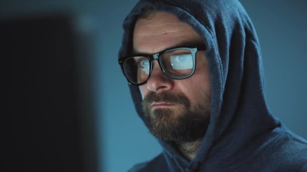 Muž hacker v kapuci a brýle pracující na počítači v temné pracovně. Koncept kyberkriminality — Stock video