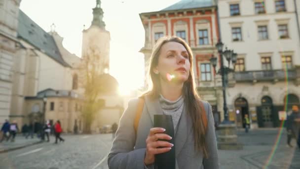 Mujer con una taza de termo en la mano caminando por la calle y mira su reloj, apresurándose a una reunión al atardecer en un frío día de otoño — Vídeos de Stock