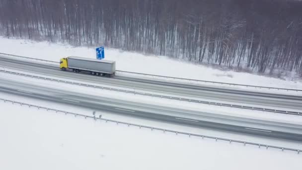 Légi kilátás a forgalom egy úton körülvett téli erdő hóesésben — Stock videók