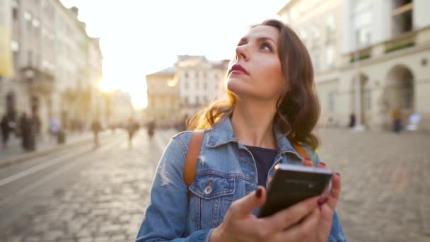 Женщина, идущая по старой улице со смартфоном и фотографирующая закат. Медленное движение — стоковое видео