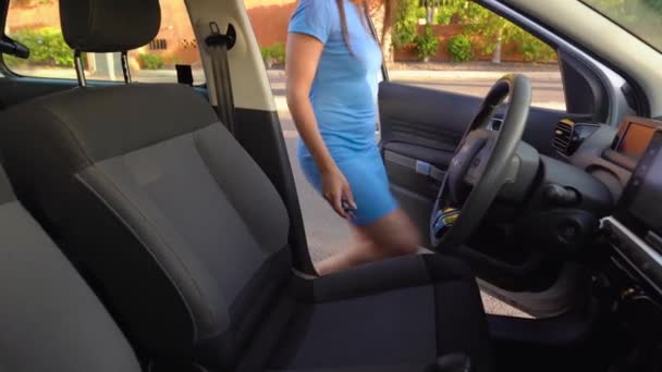 青いドレスの女性は、車の中に座って、彼女のシートベルトを締結し、運転する前に点火キーを置きます — ストック動画
