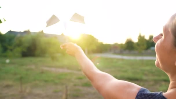 Γυναίκα εκτοξεύει χάρτινο αεροπλάνο με φόντο το ηλιοβασίλεμα. Ονειρεύομαι ταξίδια ή το επάγγελμα μιας αεροσυνοδού. Αργή κίνηση — Αρχείο Βίντεο