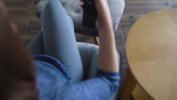 Vrouw zit in een stoel, TV kijken met een groen scherm, schakelen kanalen met een afstandsbediening. Chroma Key. Binnen — Stockvideo