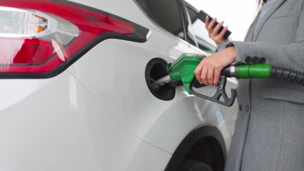Woman using smartphone while her car is refueling. Slow motion — Stock Video