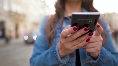 Gün batımında akıllı telefon kullanarak eski bir caddede yürüyen bir kadın. Yakın plan. Ağır çekim. İletişim, sosyal ağlar, online alışveriş kavramı