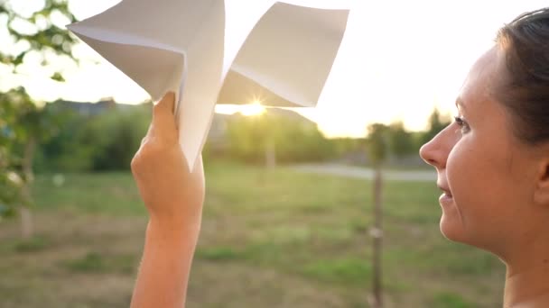 Vrouw lanceert papieren vliegtuig tegen zonsondergang achtergrond. Dromen van reizen of het beroep van stewardess. Langzame beweging — Stockvideo