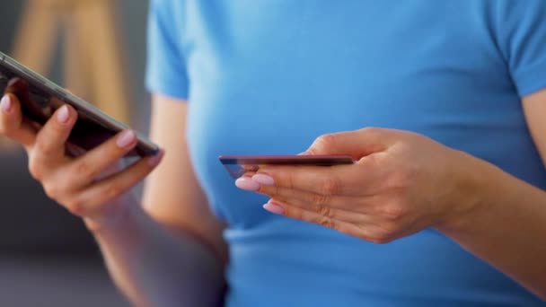 Mulher senta-se em um sofá e insere um número de cartão de crédito em um smartphone para pagar online. Compras online, tecnologia de estilo de vida. Close-up — Vídeo de Stock