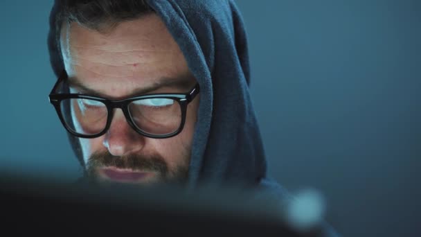 Мужчина-хакер в капюшоне и очки, работающие на компьютере в темной офисной комнате. Концепция киберпреступлений — стоковое видео