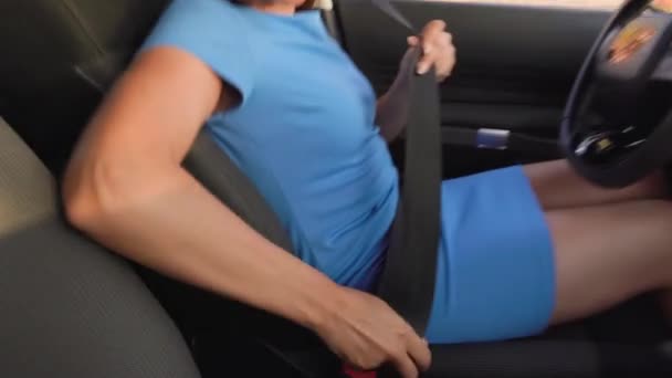 Женщина в синем платье садится в машину, пристегивает ремень безопасности и кладет руки на руль перед вождением — стоковое видео