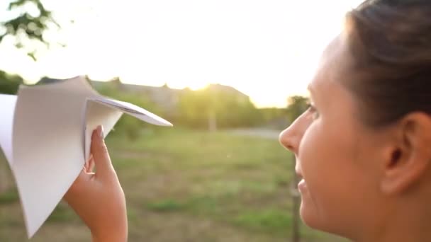 Vrouw lanceert papieren vliegtuig tegen zonsondergang achtergrond. Dromen van reizen of het beroep van stewardess. Video werd opgenomen op verschillende snelheden - normaal en langzaam — Stockvideo