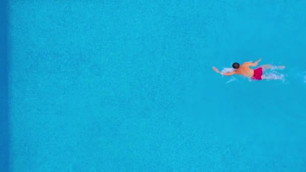 Aerial view of man in red shorts swims in the pool. Slow motion — 비디오