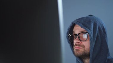 Kapüşonlu ve gözlüklü bir erkek hacker karanlık bir ofis odasında bilgisayar üzerinde çalışıyor. Siber suç kavramı